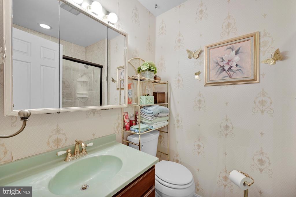 Bathroom with pale green vanity, patterned wallpaper, and glass shower reflected in the mirror.