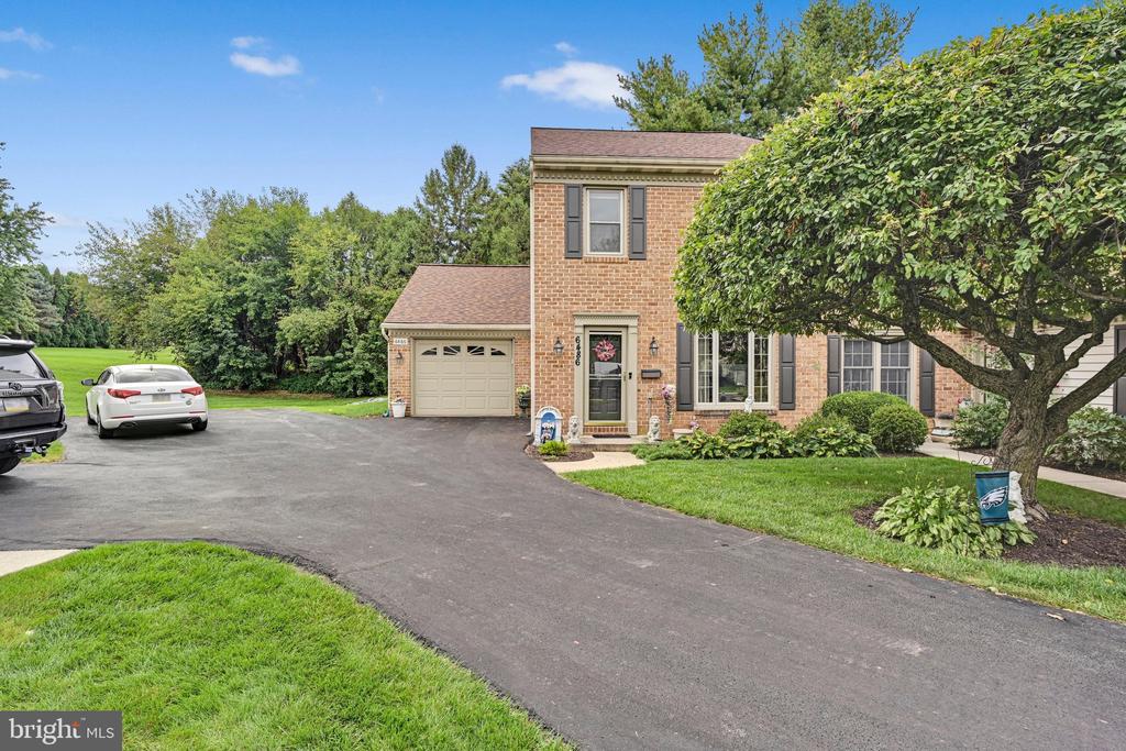 Two-story brick home with an attached garage, wide driveway, and mature tree in the front yard.