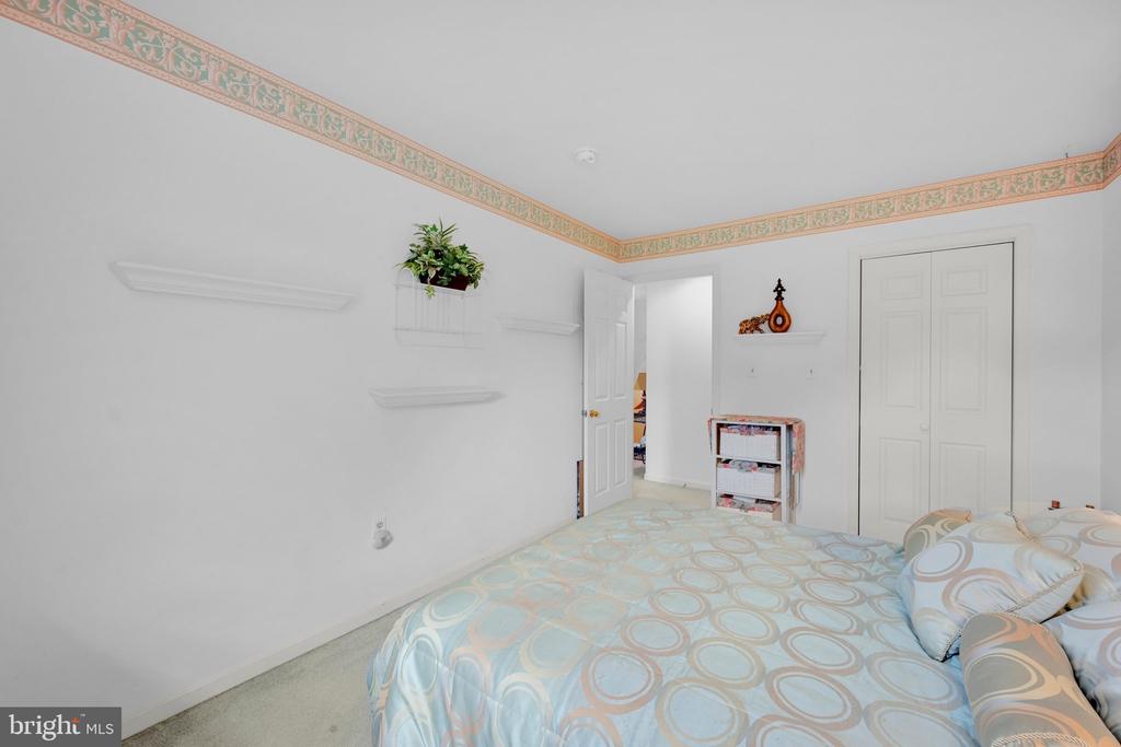 Bedroom with pale blue patterned bedding, decorative wallpaper border, wall shelves, and a double-door closet.