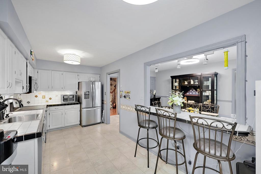 Kitchen with white cabinets and stainless steel appliances beside a dining counter with metal stools.