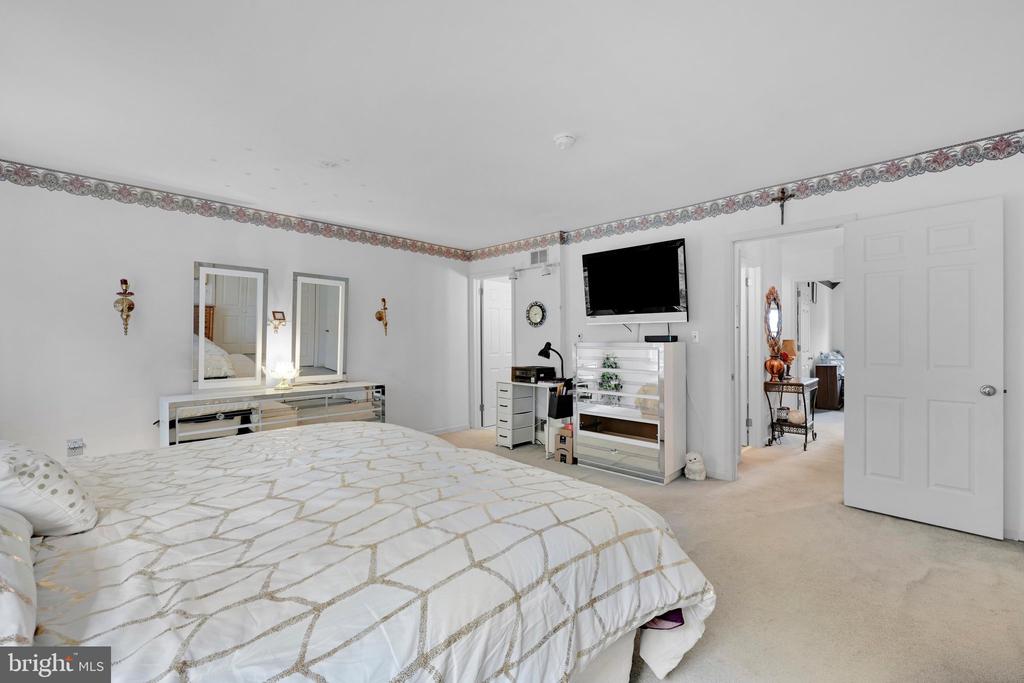 Furnished bedroom with a geometric-patterned bedspread, mirrored furniture, and a wall-mounted TV.