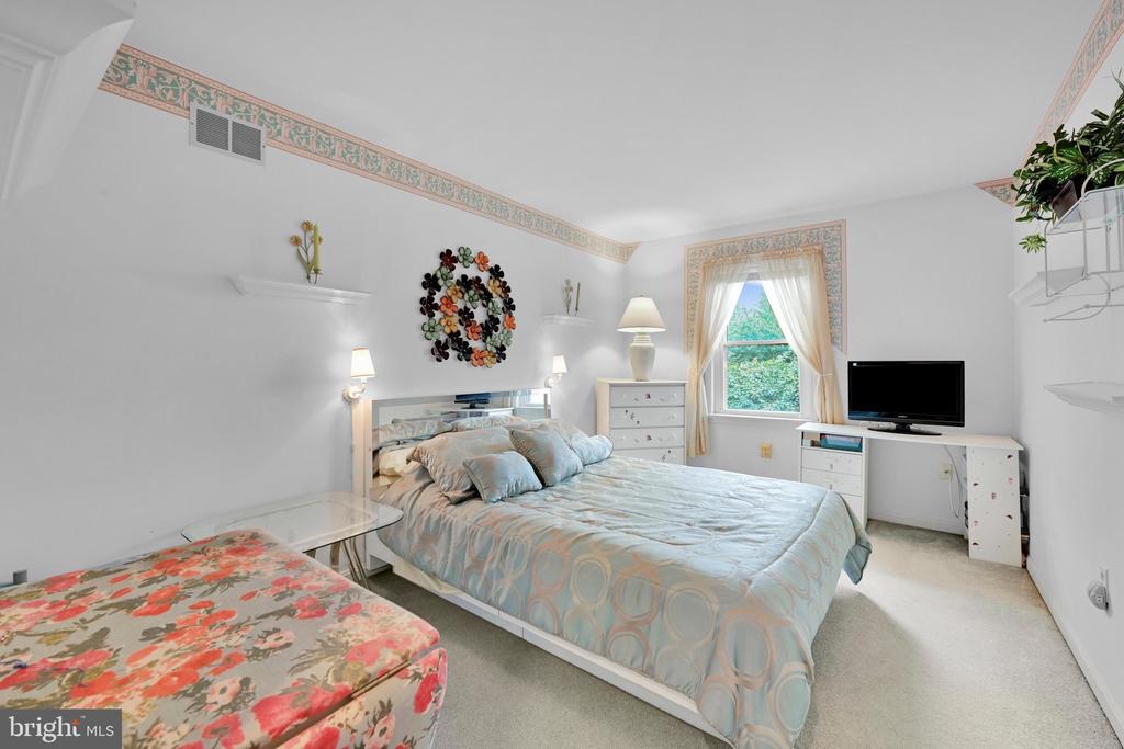 Bedroom with a large bed, floral bench, and window overlooking greenery.