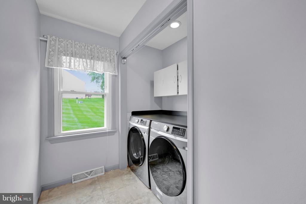 Laundry room with front-loading washer and dryer, wall cabinets, and a window overlooking the lawn.