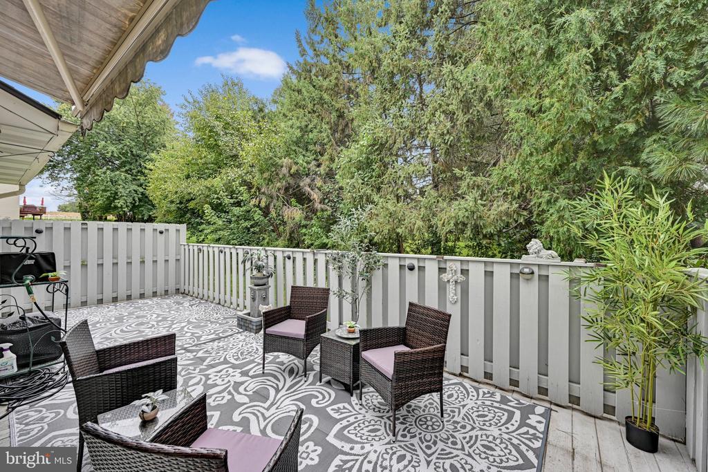 Furnished deck with wicker seating, a patterned rug, and trees beyond the railing.