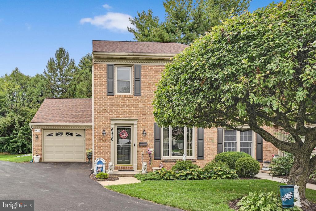 Two-story brick home with an attached garage, mature landscaping, and a large shade tree.