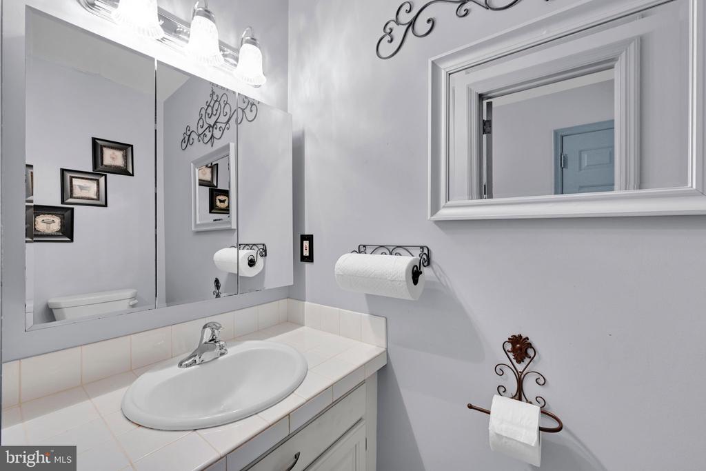 Bathroom vanity with an oval sink, tiled countertop, mirrored cabinet, and decorative towel holders.