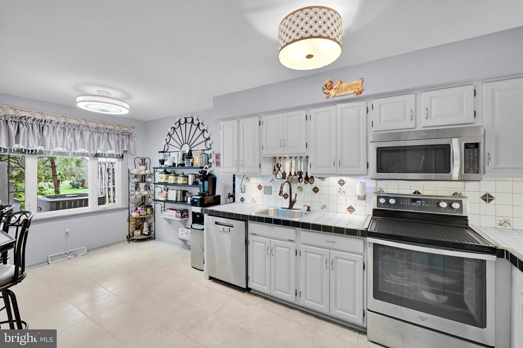 Kitchen with white cabinets, black countertops, stainless steel appliances, and a large yard-facing window.