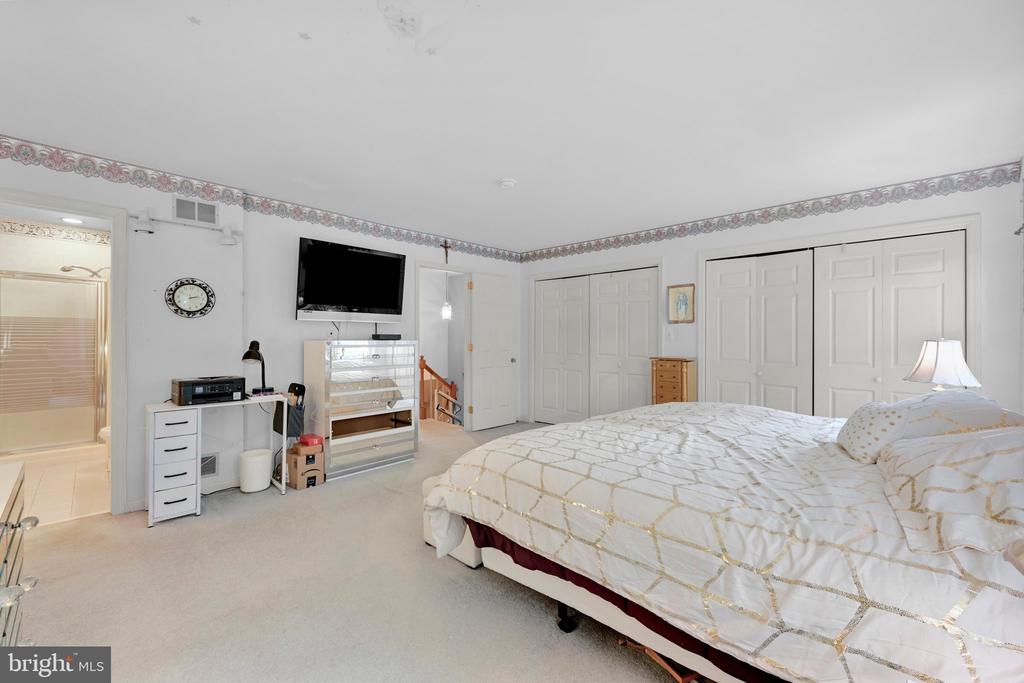 Bedroom with a large white-quilted bed, wall-mounted television, glass display cabinet, and multiple closets.