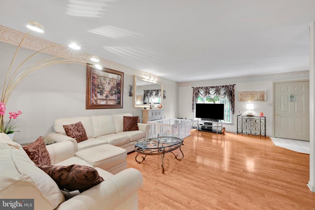 Living room with white sectional sofas, hardwood floors, and a playpen by the window.