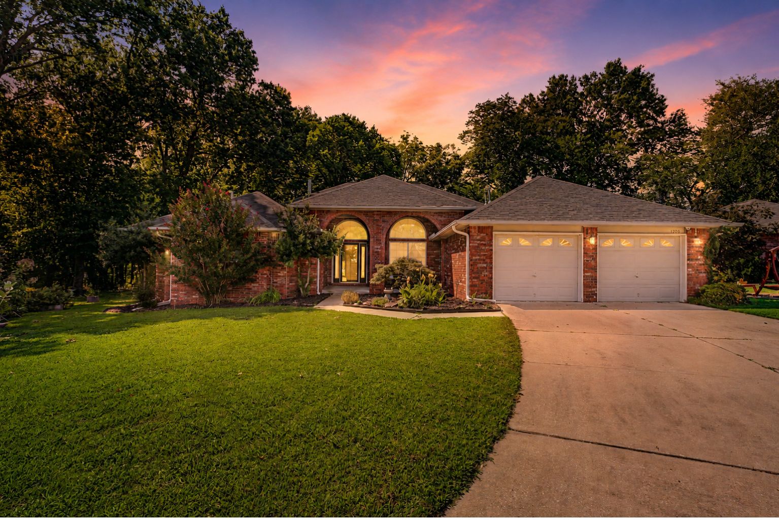 Red brick home with arched windows and a double garage, lit at dusk.