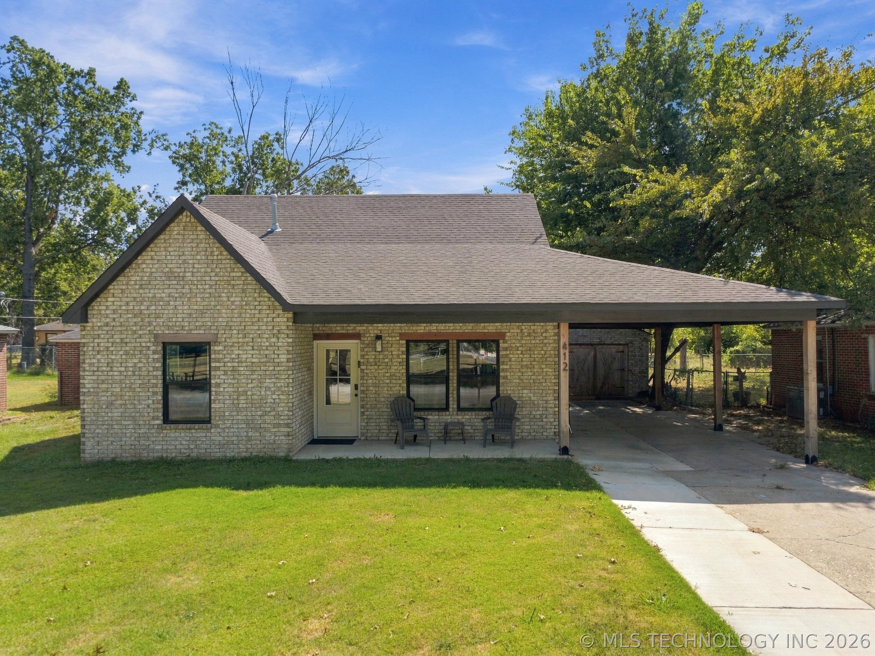 Brick home with a covered carport, porch chairs, and a broad green lawn.