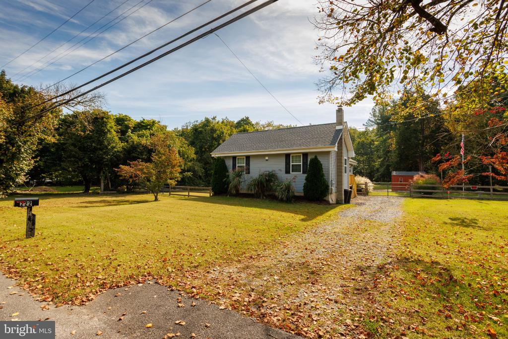 Single-story home beyond a leaf-strewn lawn and gravel driveway, surrounded by mature autumn trees.