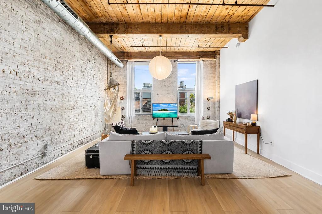 Staged loft living room with exposed brick walls, a timber ceiling, and large windows.
