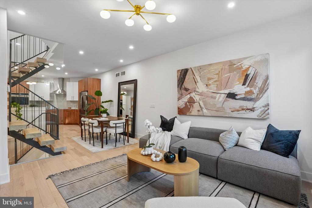 Open-plan living room with a gray sectional, abstract wall art, and floating staircase.