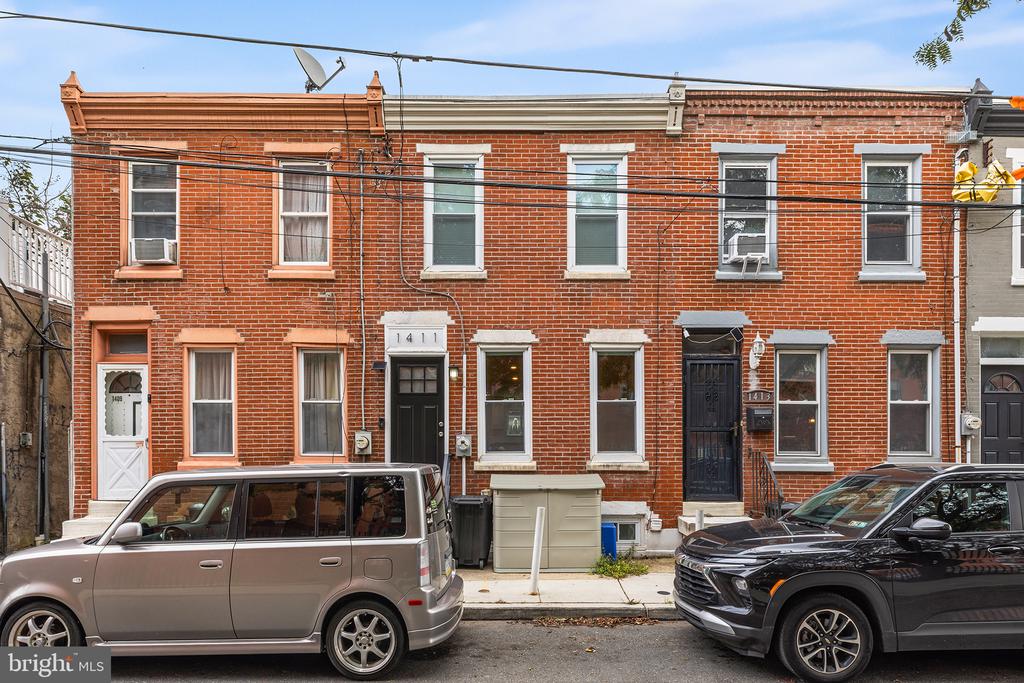 Red-brick rowhouse exterior with white-trimmed windows, front stoops, and parked cars.
