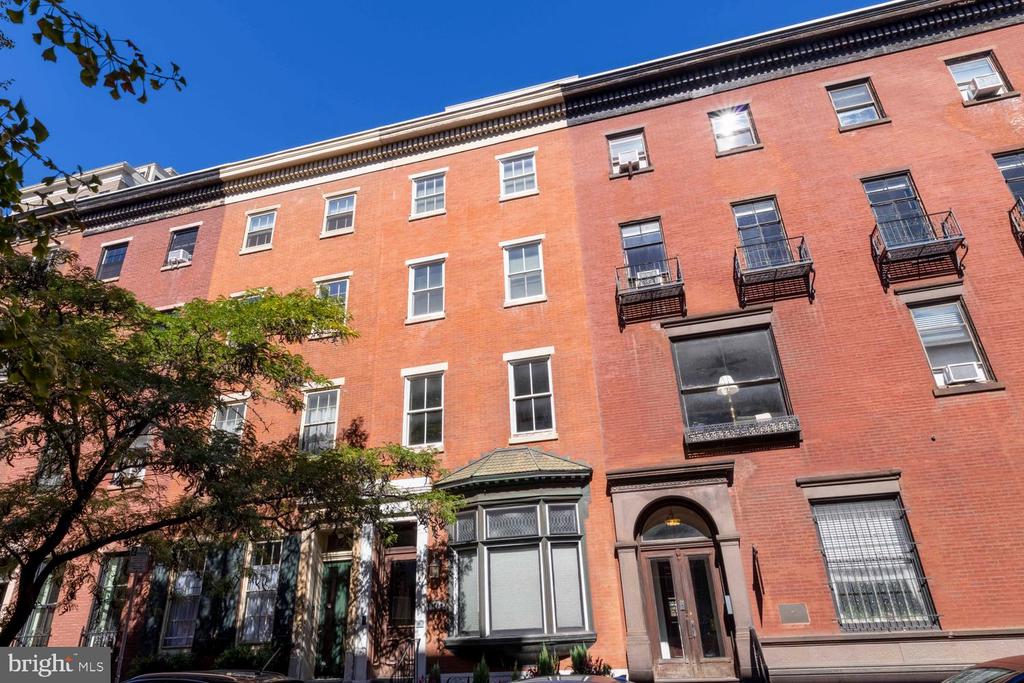 Red brick row building with iron balconies, bay windows, and an arched entrance.