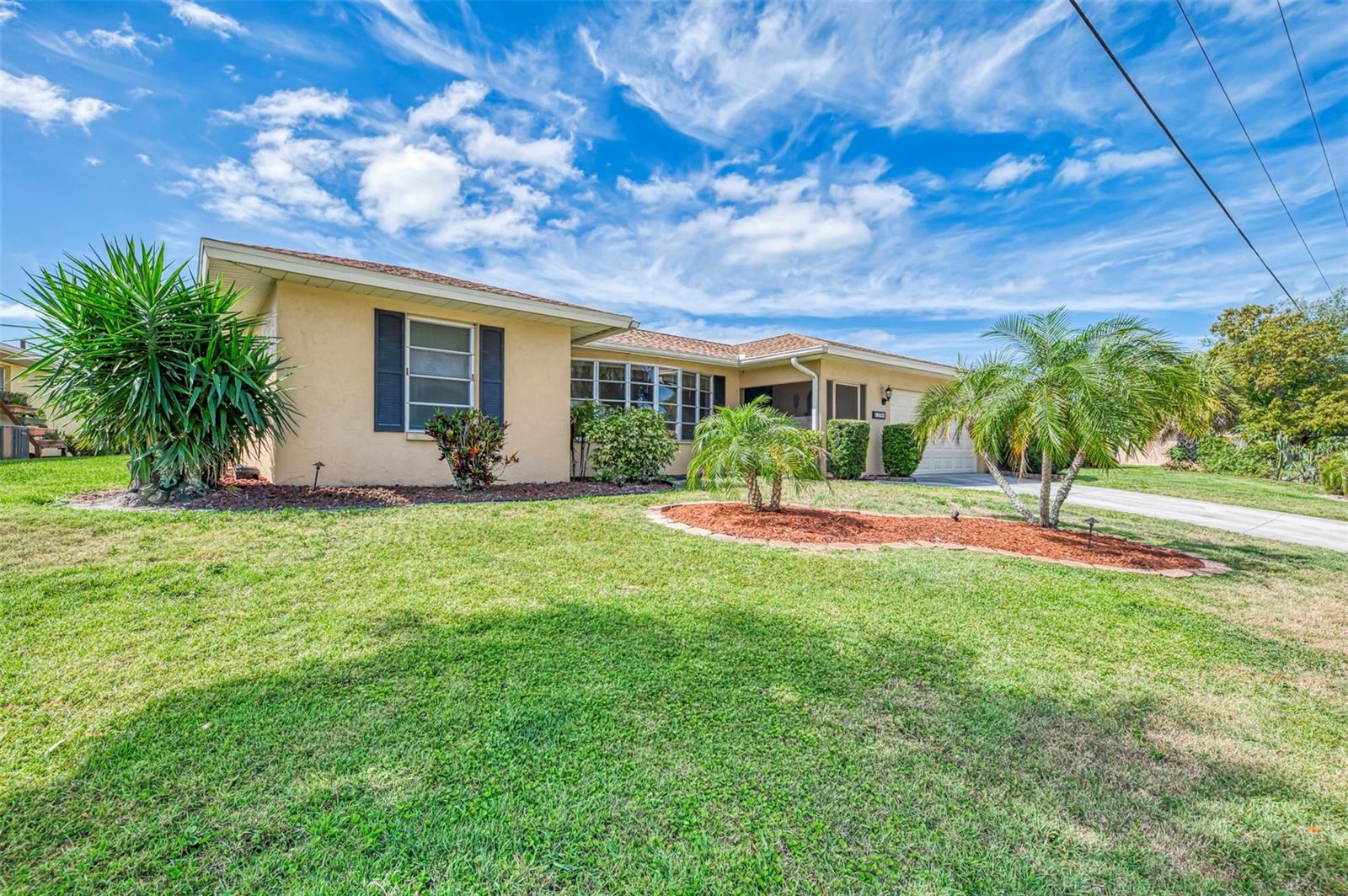 Single-story beige home with a tiled roof, attached garage, and tropical palms along the front lawn.