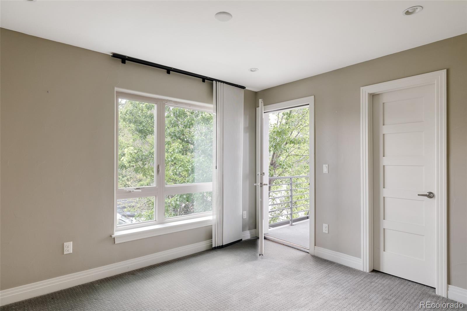 Empty bedroom with a large leafy-view window and an open door to a balcony.