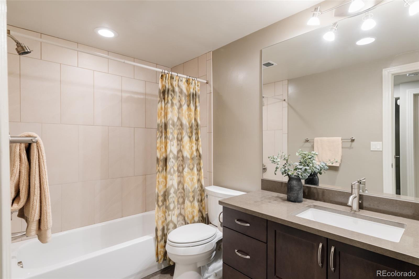 Bathroom with a tiled tub and shower, patterned curtain, and dark vanity.