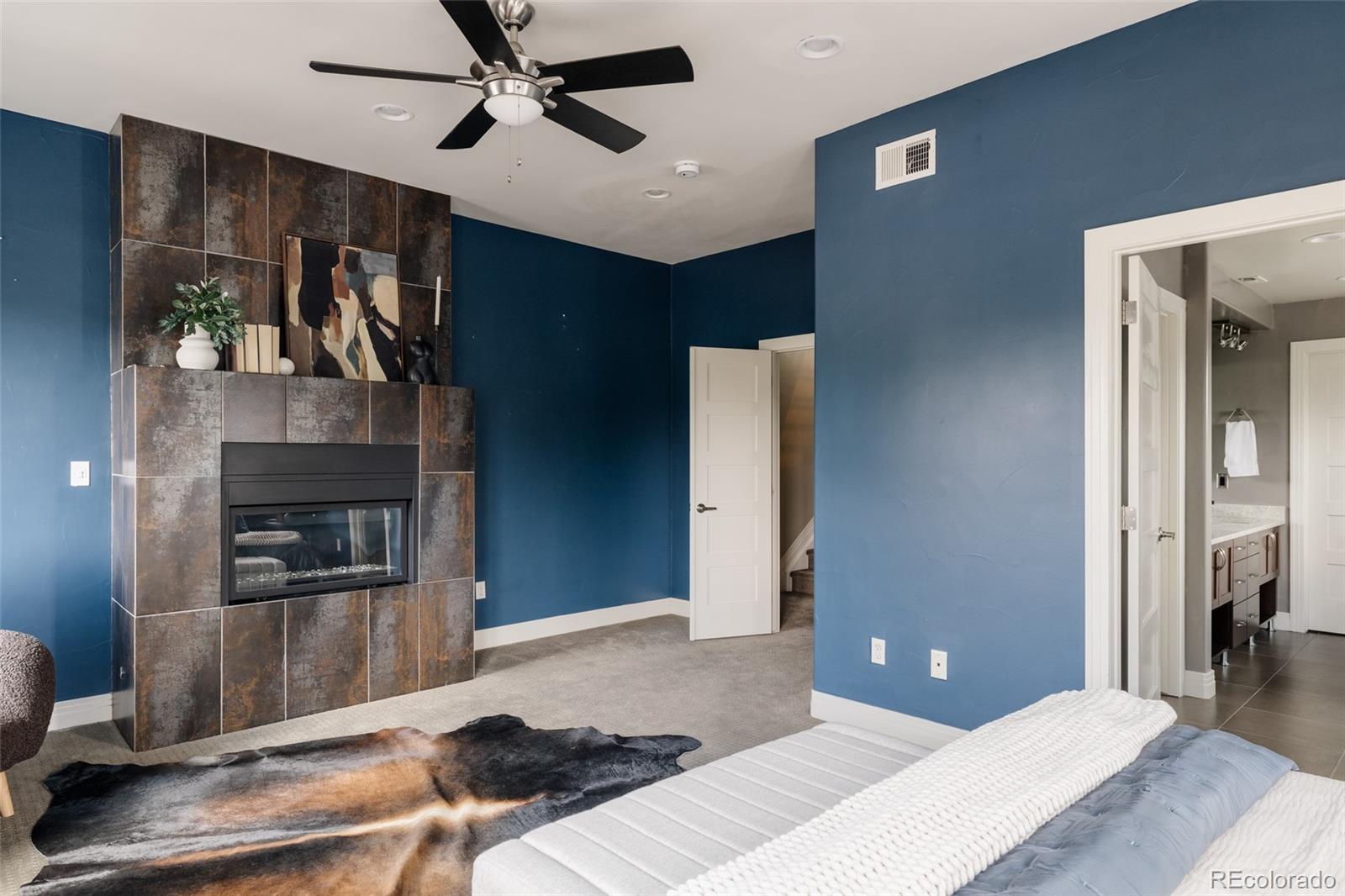 Furnished bedroom with blue walls, a tiled fireplace, and an open doorway to the en-suite bathroom.