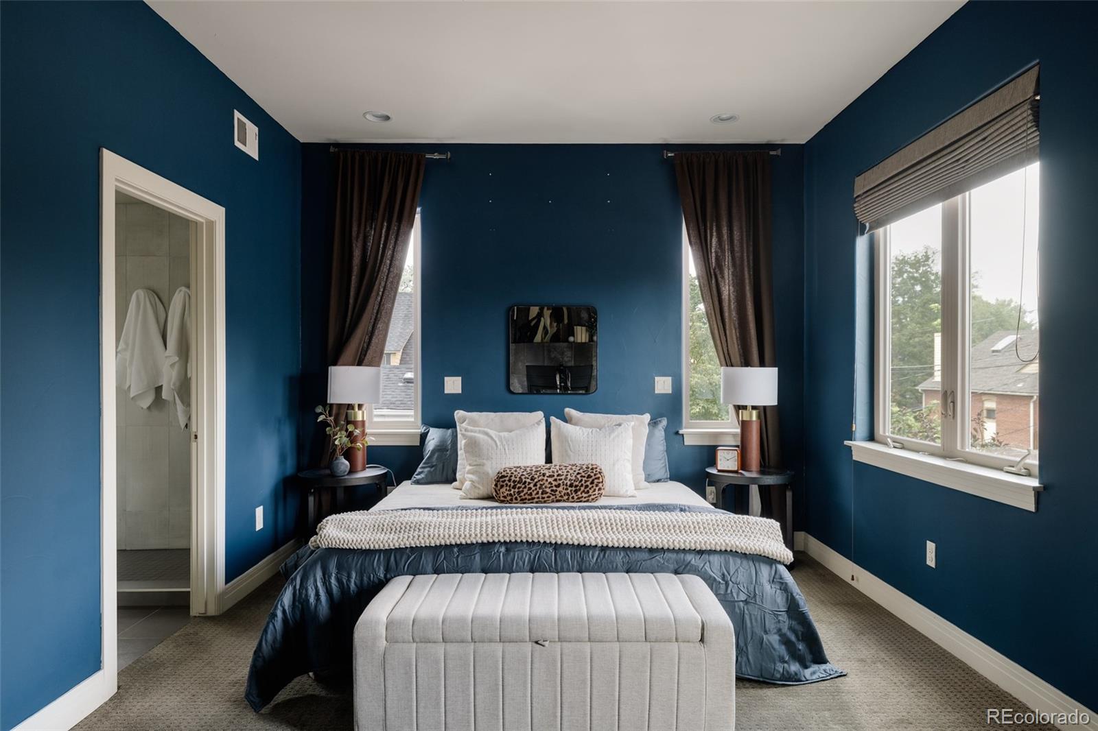 Furnished bedroom with deep blue walls, a white-pillowed bed, and an upholstered bench.