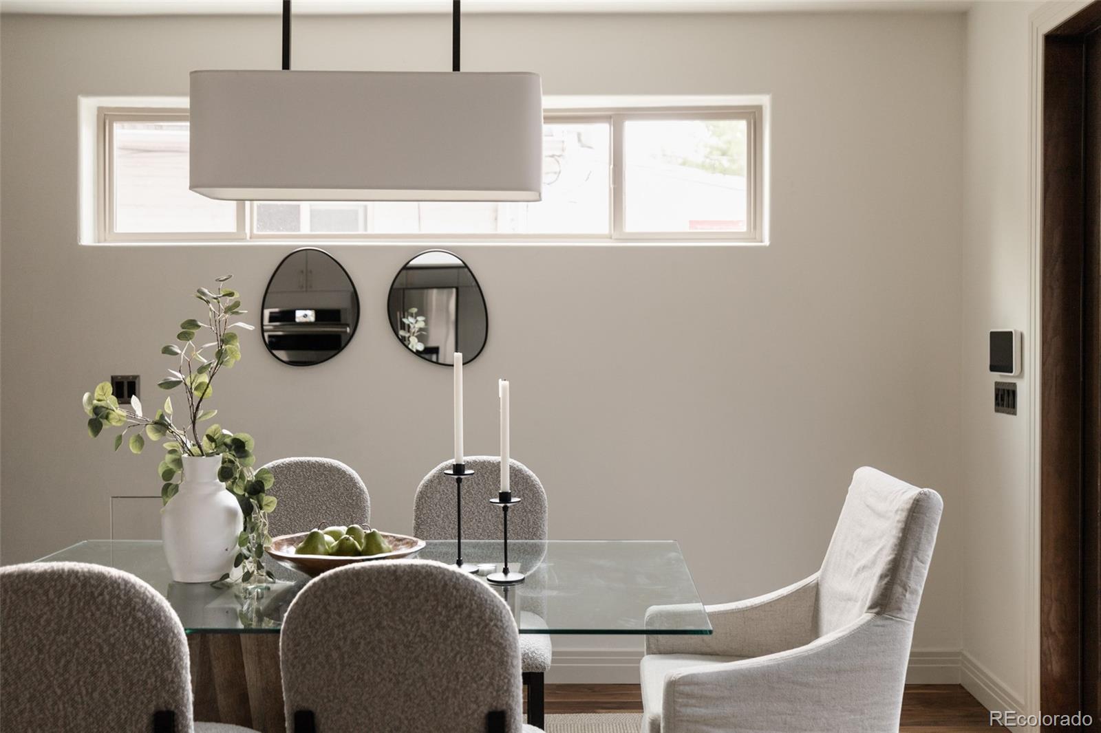 Dining room with a glass-top table, upholstered chairs, and a large rectangular pendant light.