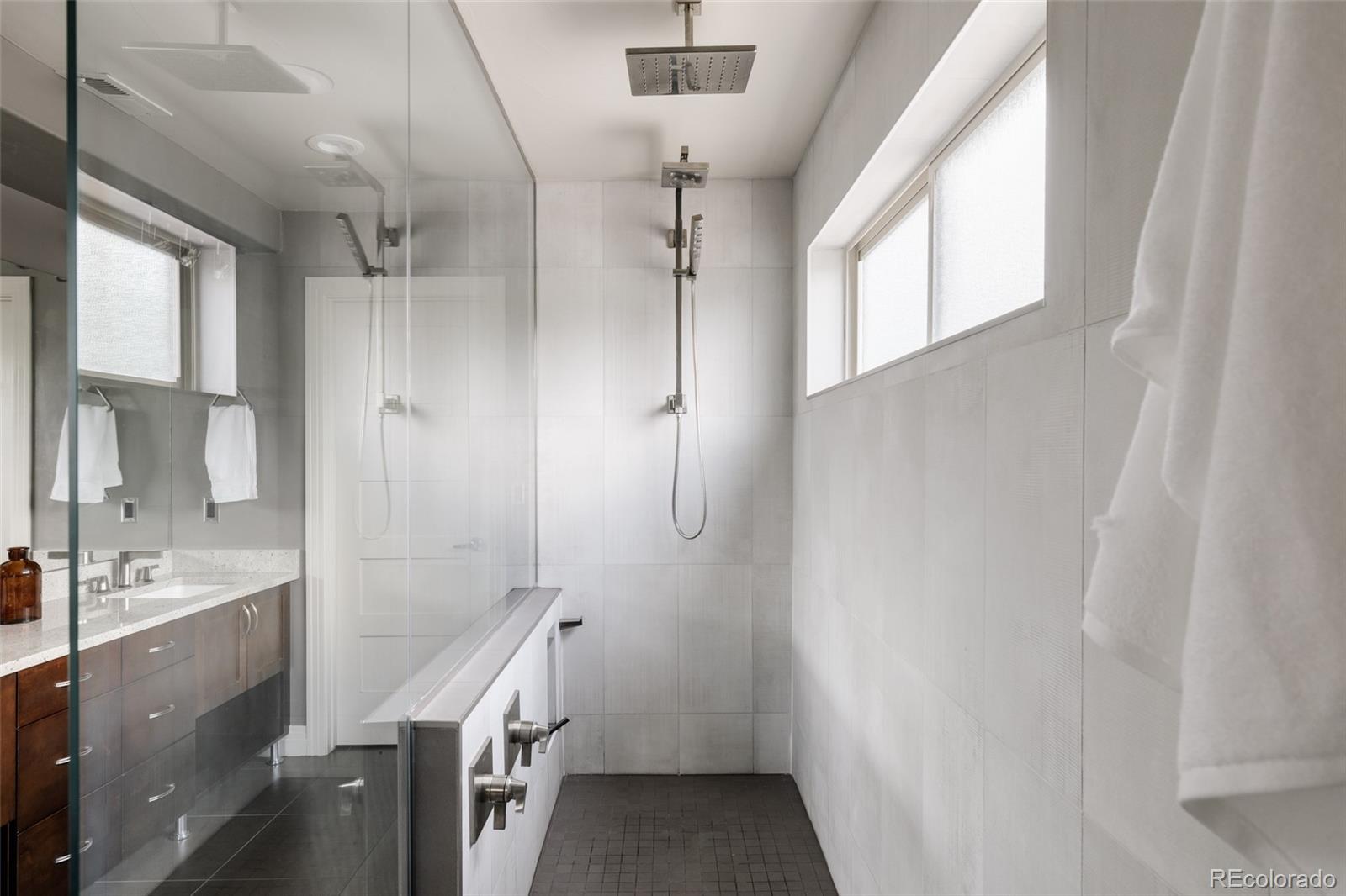 Modern tiled bathroom with a glass walk-in shower, dual showerheads, and large windows.