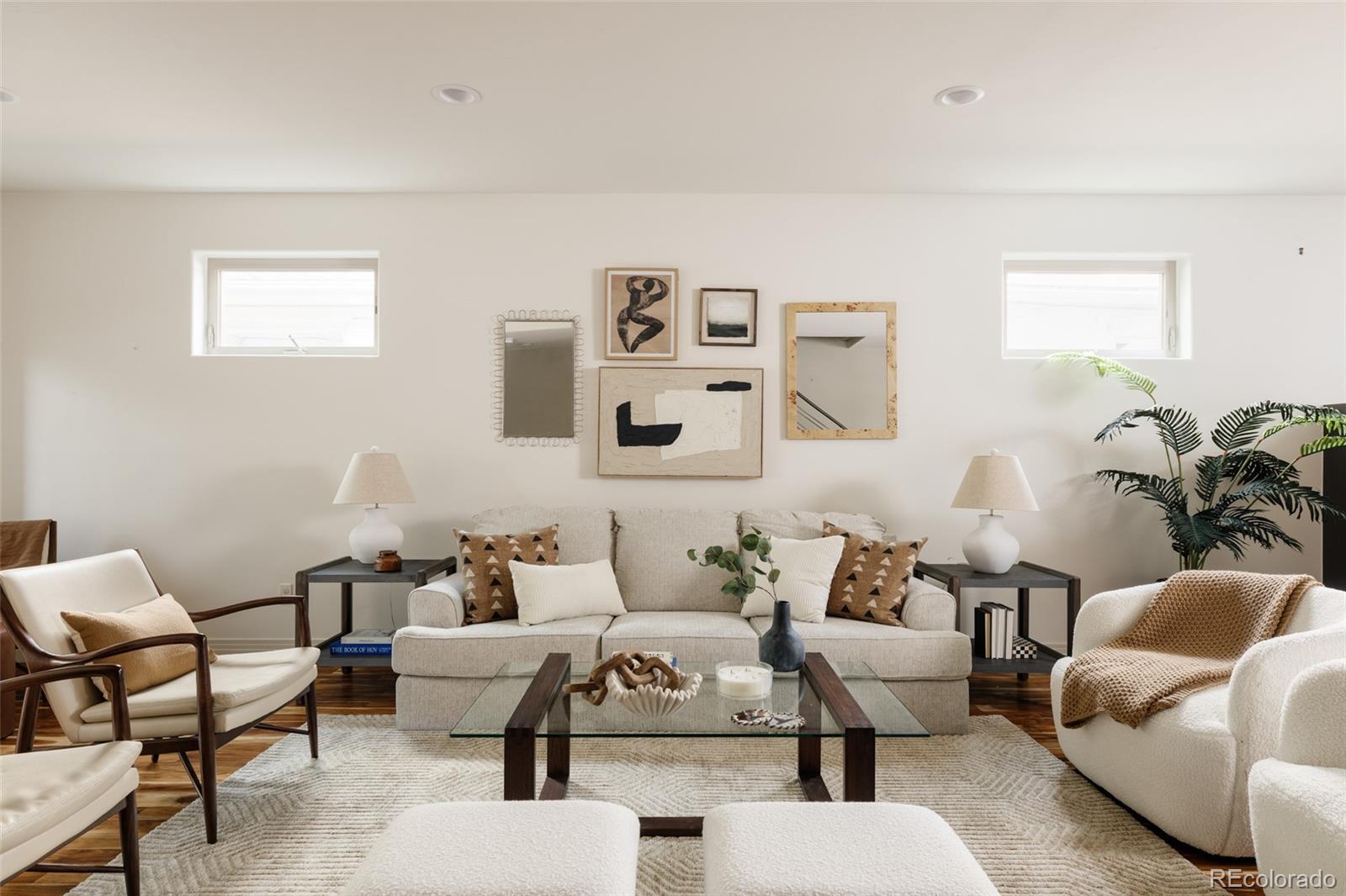 Staged living room with a cream sofa, glass coffee table, hardwood floors, and framed art.