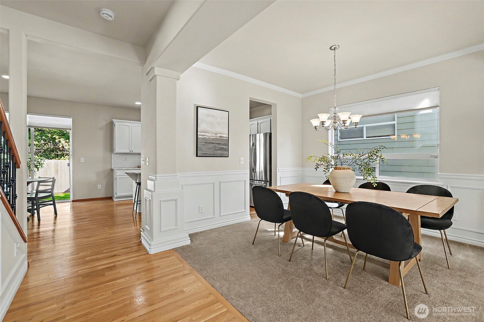 Dining room with a wooden table and black chairs beside an open kitchen.