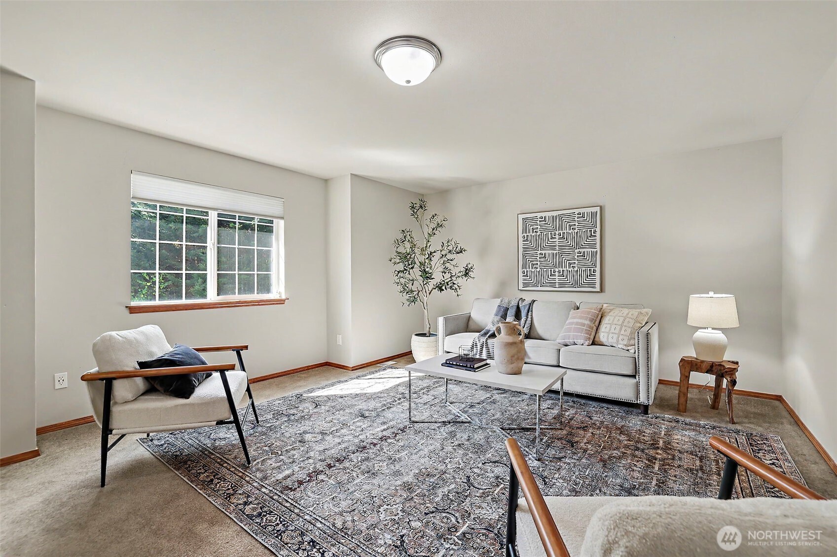 Staged living room with a gray sofa, patterned rug, and large daylight-filled window.