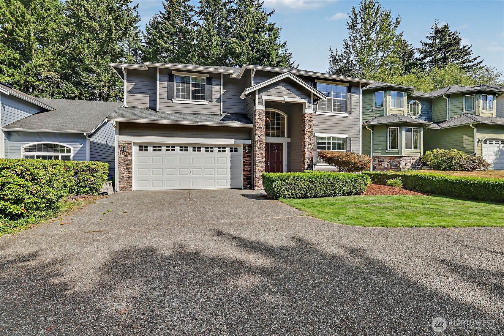 Two-story gray house with stone entry columns, double garage, wide driveway, and trimmed hedges.