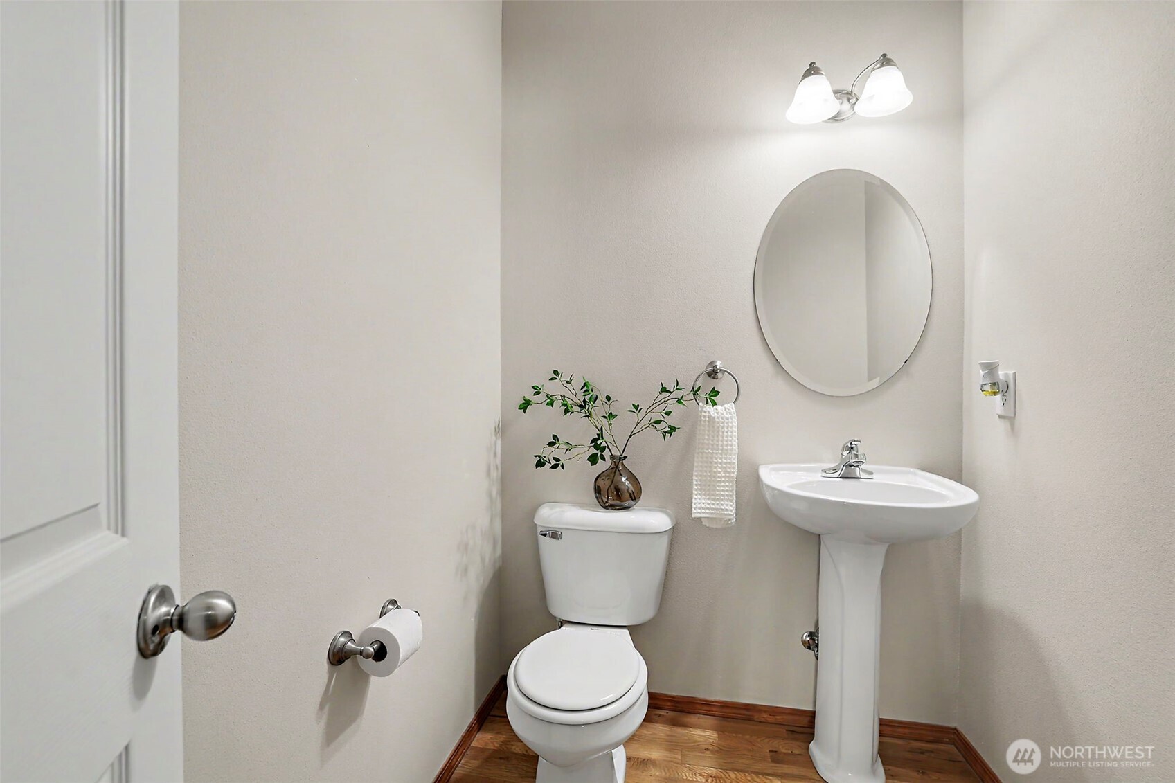 Bathroom with a white pedestal sink, oval mirror, and wood-look flooring.
