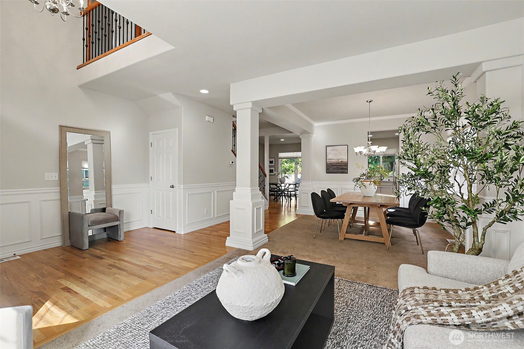 Open-plan living and dining room with hardwood floors, white wall paneling, and a staircase.