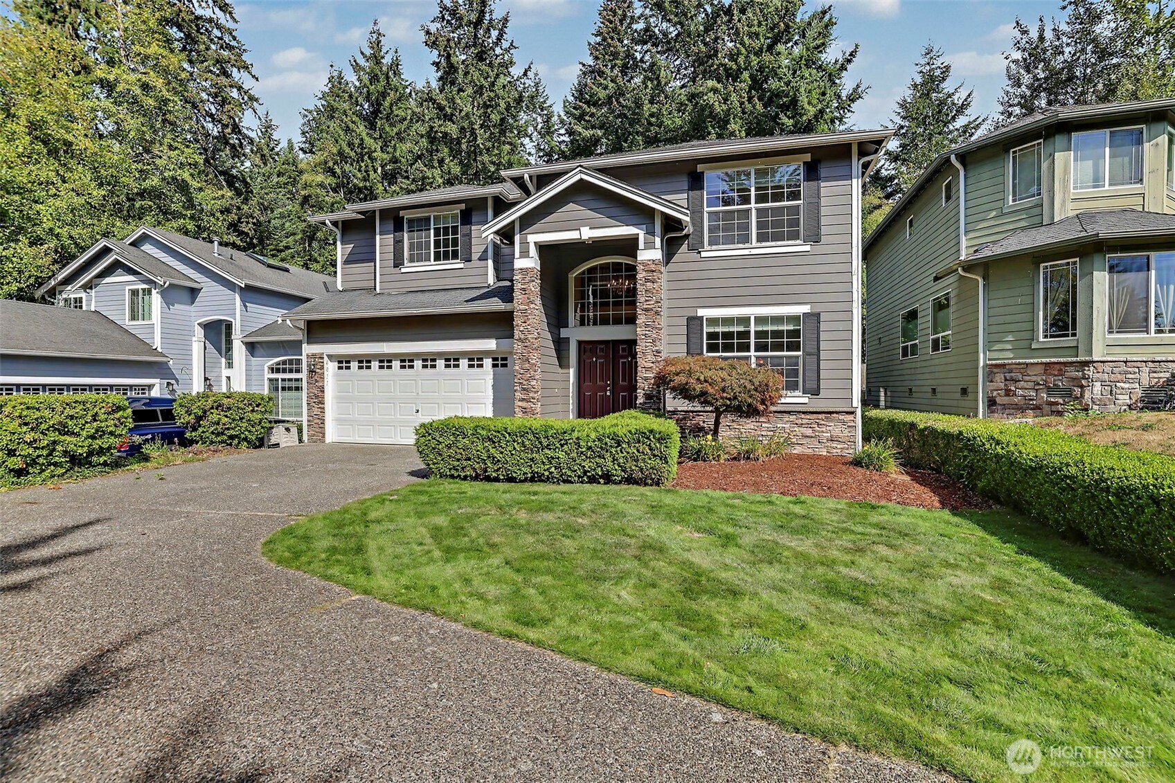 Two-story gray house with stone entry accents, a two-car garage, and a curved front lawn.