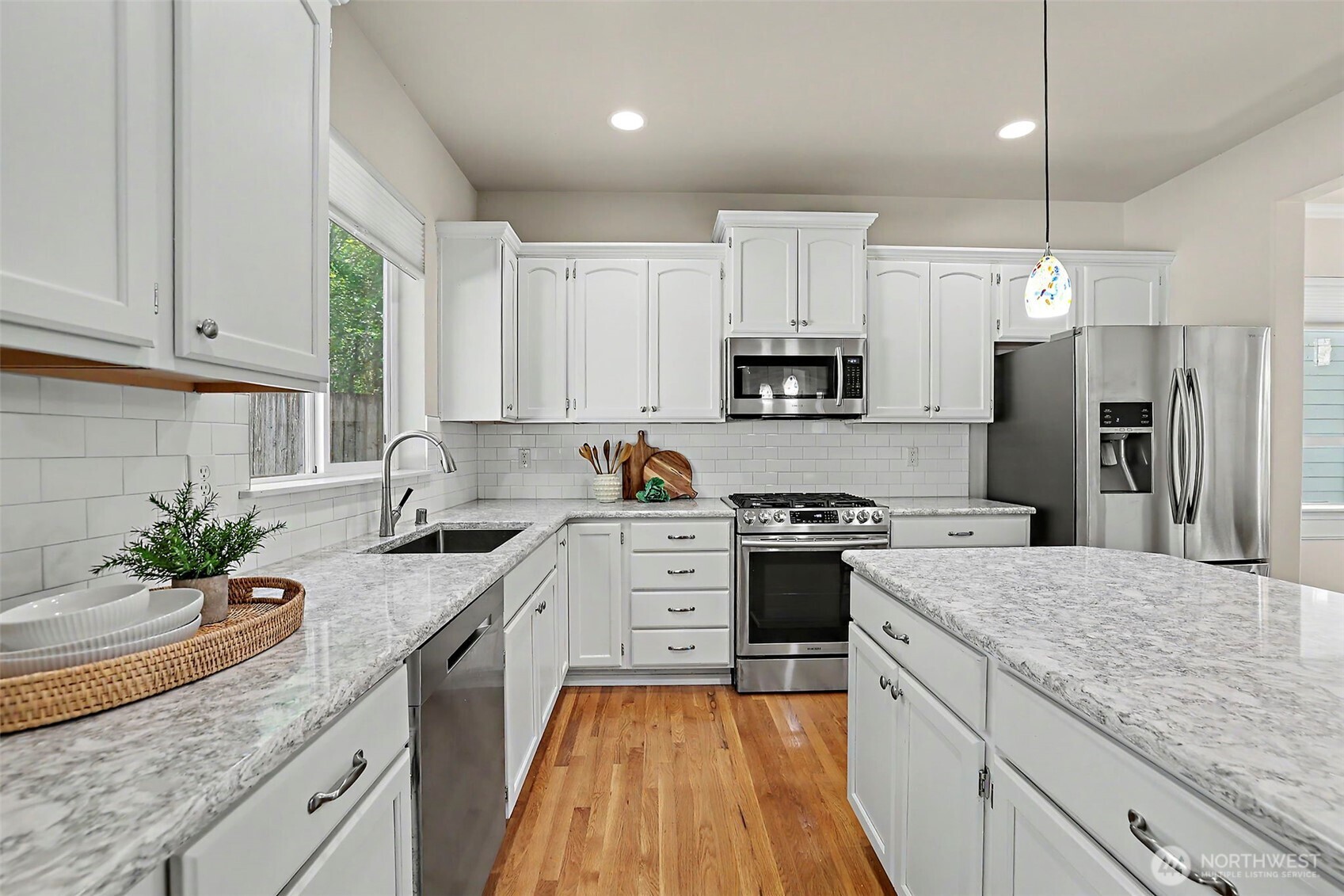 Bright kitchen with white cabinets, granite counters, a large island, stainless steel appliances, and hardwood floors.