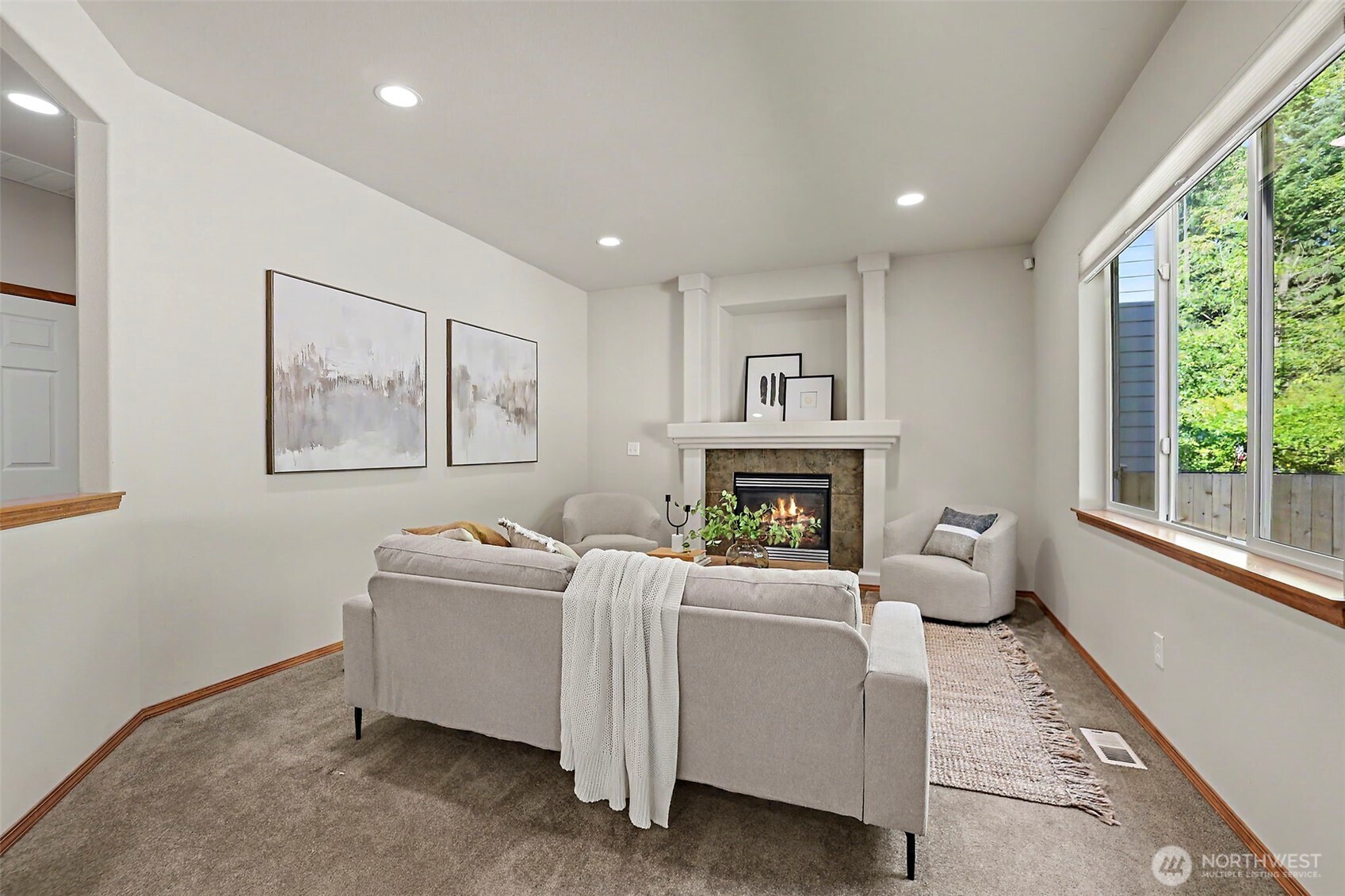 Staged living room with a gas fireplace and large window overlooking greenery.