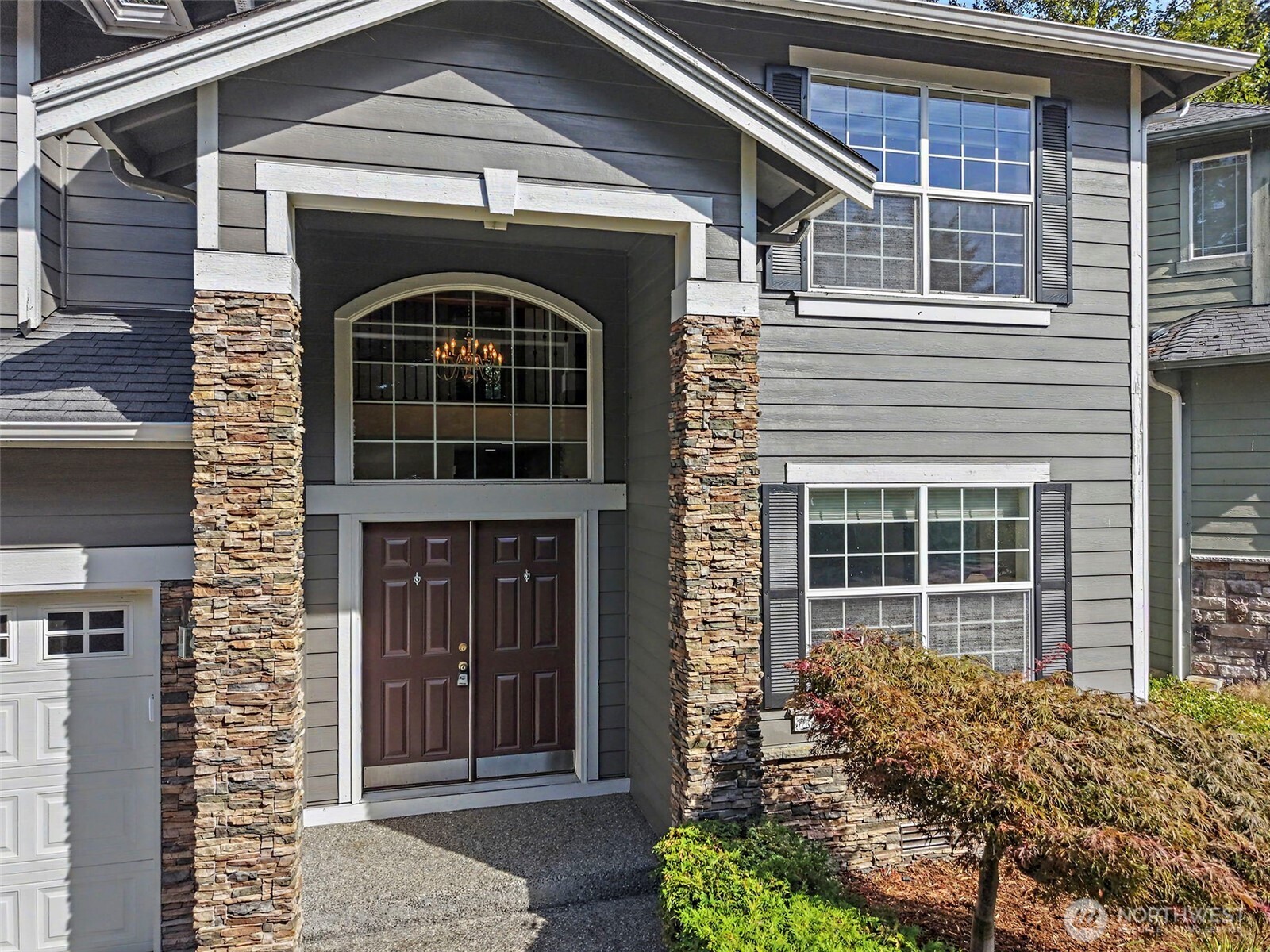 Gray two-story home with stone porch columns and dark double entry doors beneath an arched window.