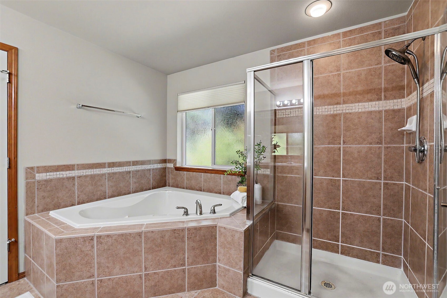 Bathroom with a corner soaking tub, tan tile, and a glass-enclosed shower.