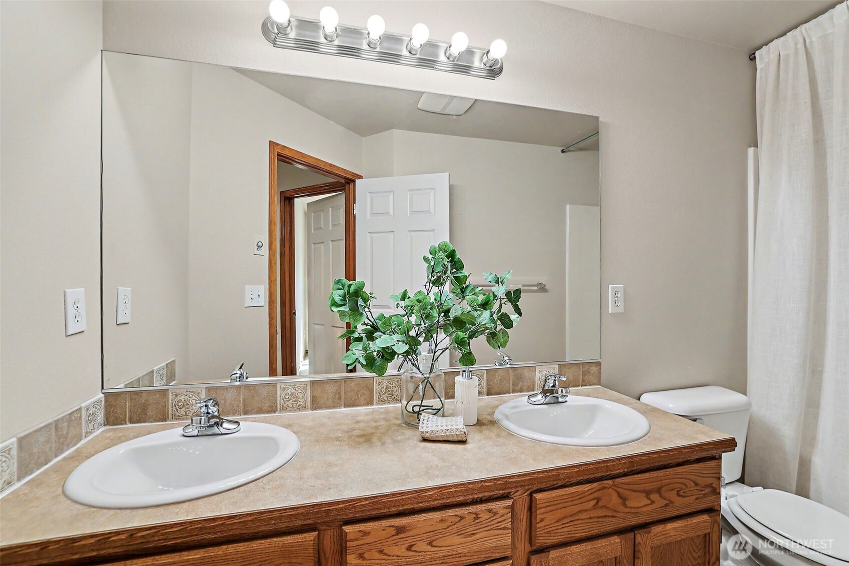 Bathroom with a double-sink wood vanity, large mirror, and decorative tile backsplash.