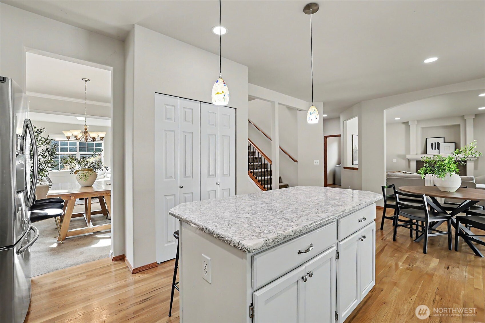 Bright kitchen with a large granite-topped island, colorful pendant lights, and adjoining dining areas.