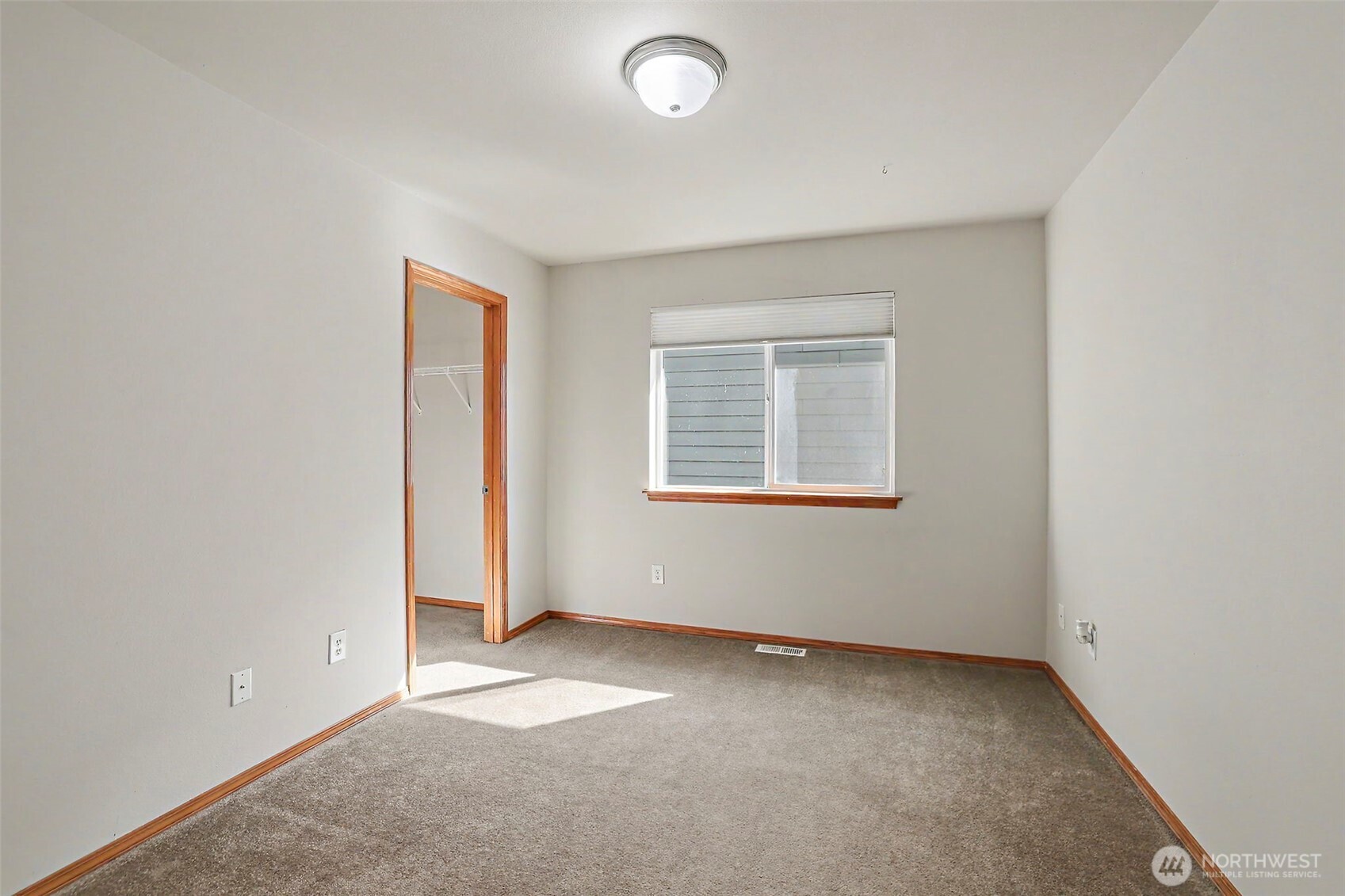 Empty bedroom with gray carpet, wood trim, a window, and an open closet doorway.