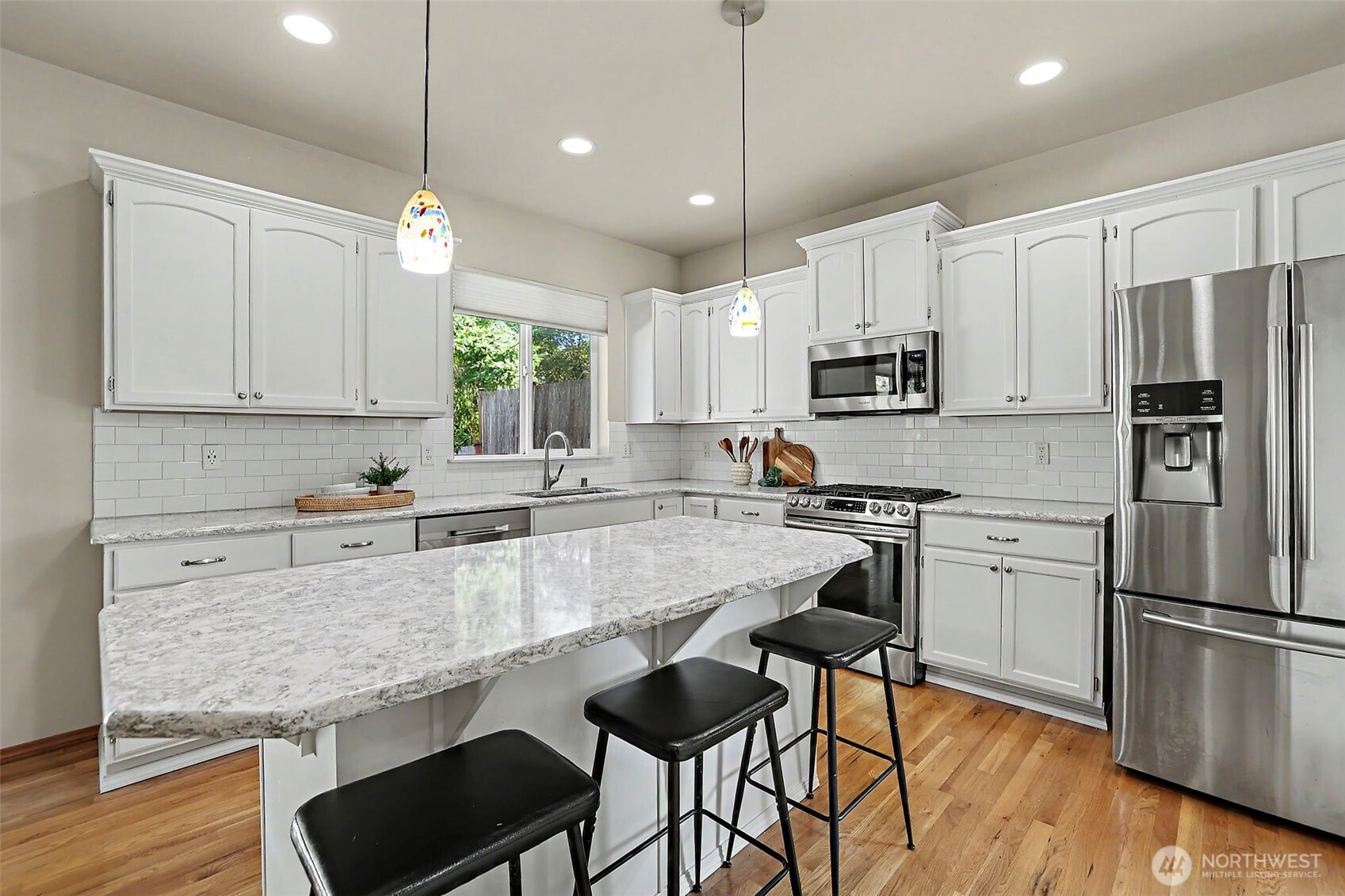 Kitchen with a large stone island, white cabinets, stainless steel appliances, and hardwood floors.