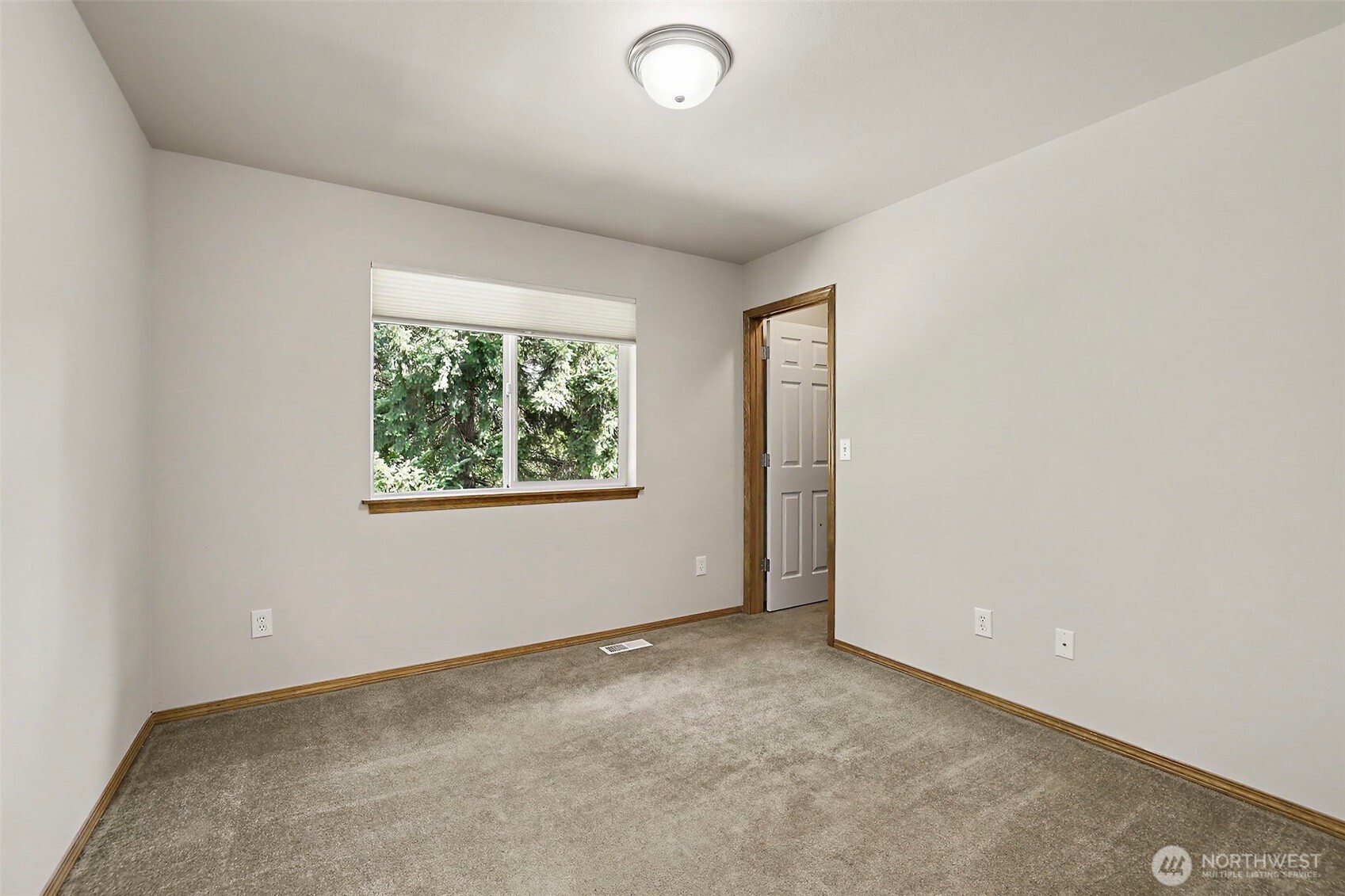 Empty carpeted room with wood trim, a window overlooking trees, and an open doorway.
