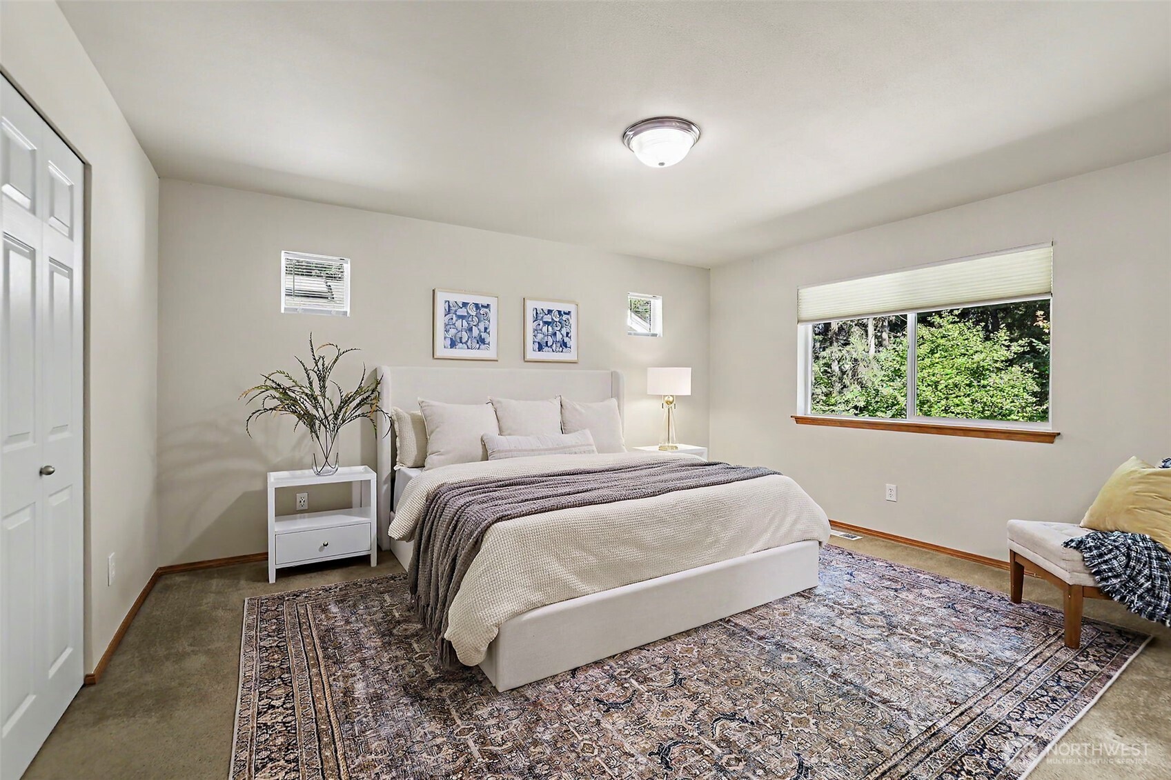 Staged bedroom with a large bed, patterned rug, and wide window overlooking greenery.