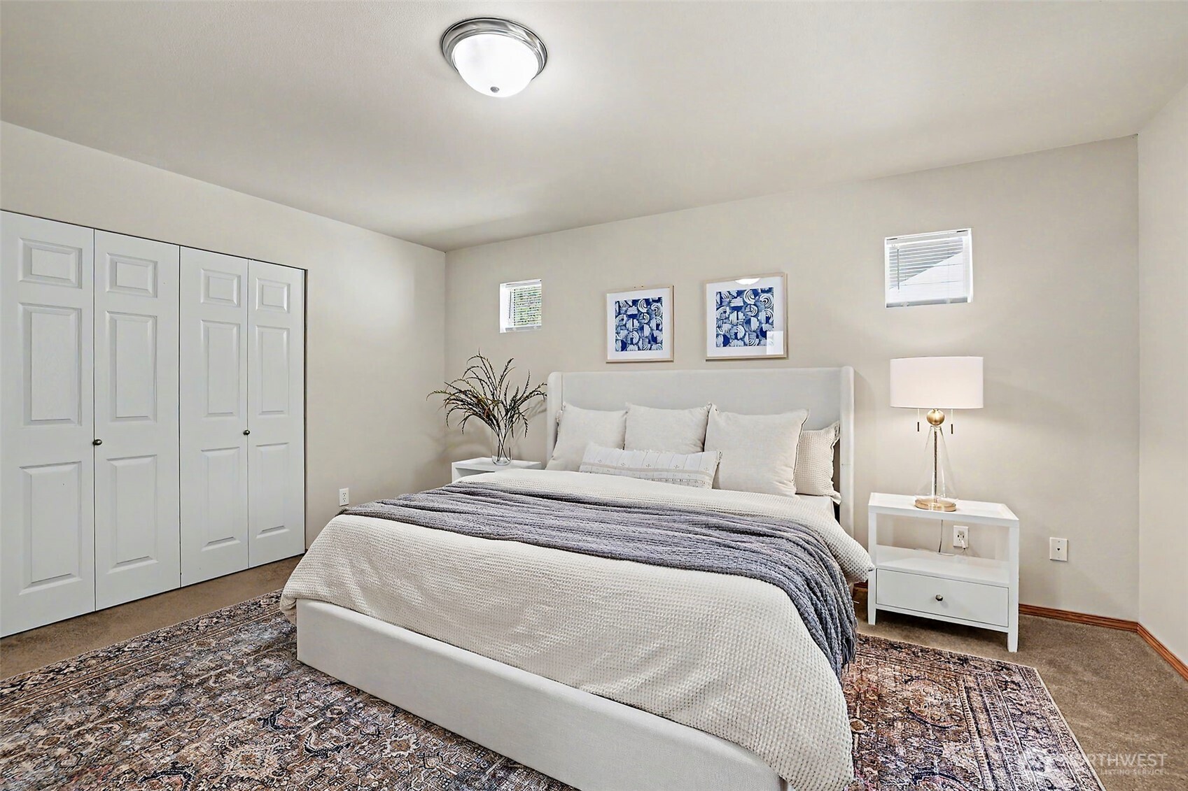 Staged bedroom with a white bed, patterned rug, and paneled closet doors.