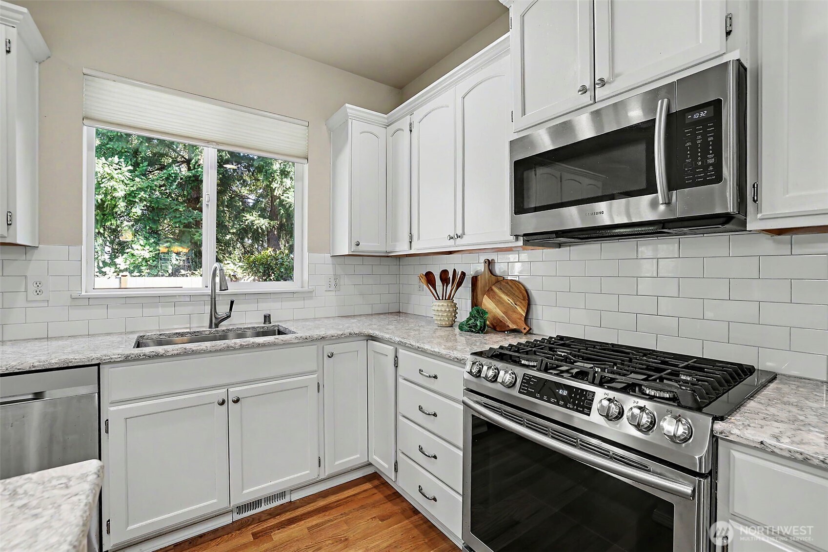 White kitchen with stainless steel range and microwave, subway tile backsplash, and a window overlooking trees.