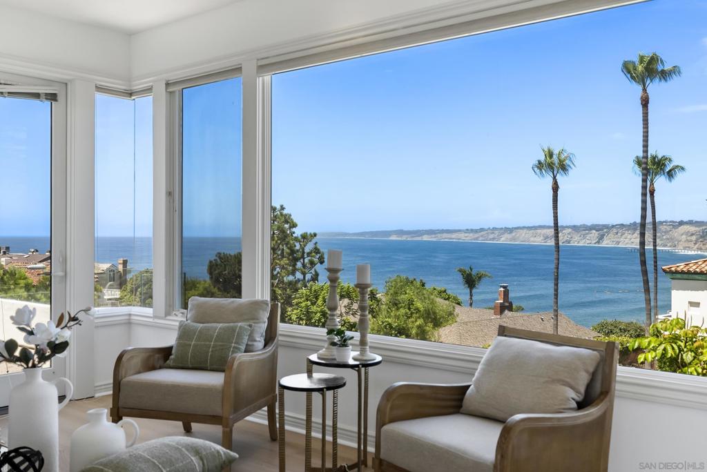 Furnished living room with wide windows overlooking the ocean and palm-lined coastline.