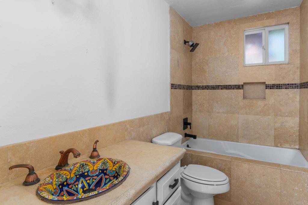 Bathroom with a colorful patterned vessel sink and tan stone tile around the bathtub.