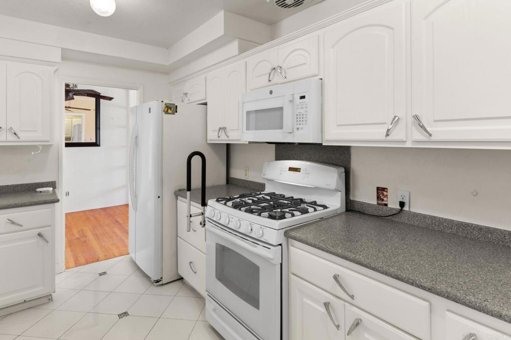 Kitchen with white cabinets, gray countertops, and a white gas range beside the refrigerator.