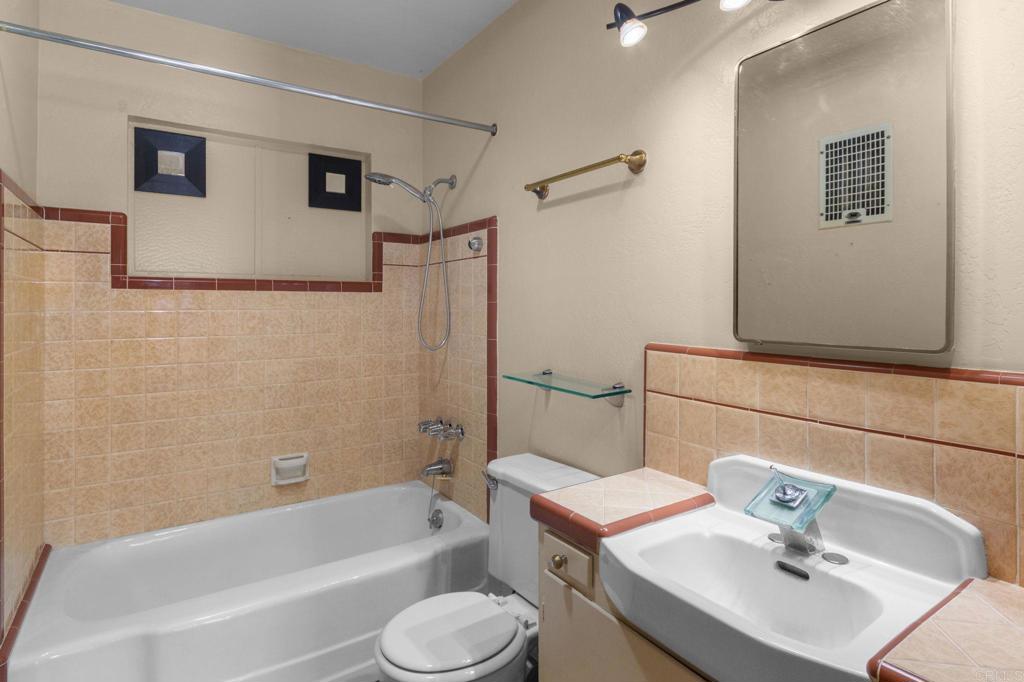 Bathroom with peach tile, a bathtub and shower, and a sink beneath a large mirror.